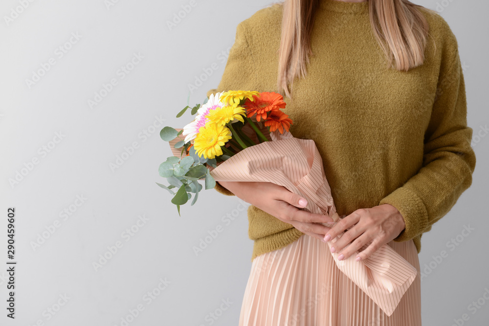 浅色背景上有一束美丽的非洲菊花的女人