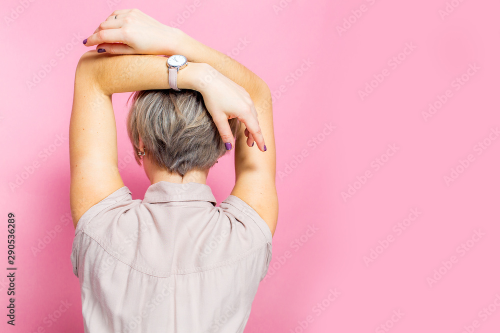 Rear view of a woman relaxing, standing and holding hands up over pink