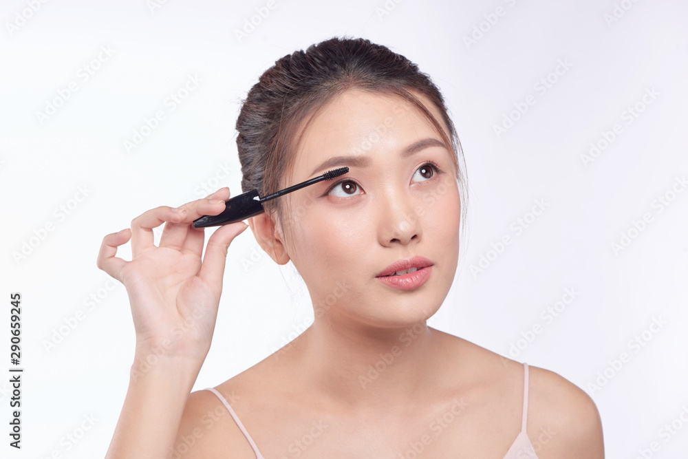 Mascara woman putting makeup on eyes. Asian female model face closeup with eye brush on eyelashes.