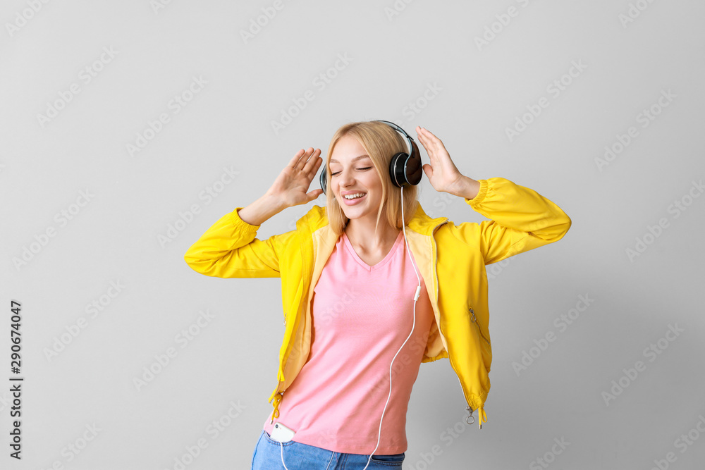 Beautiful young woman listening to music on light background