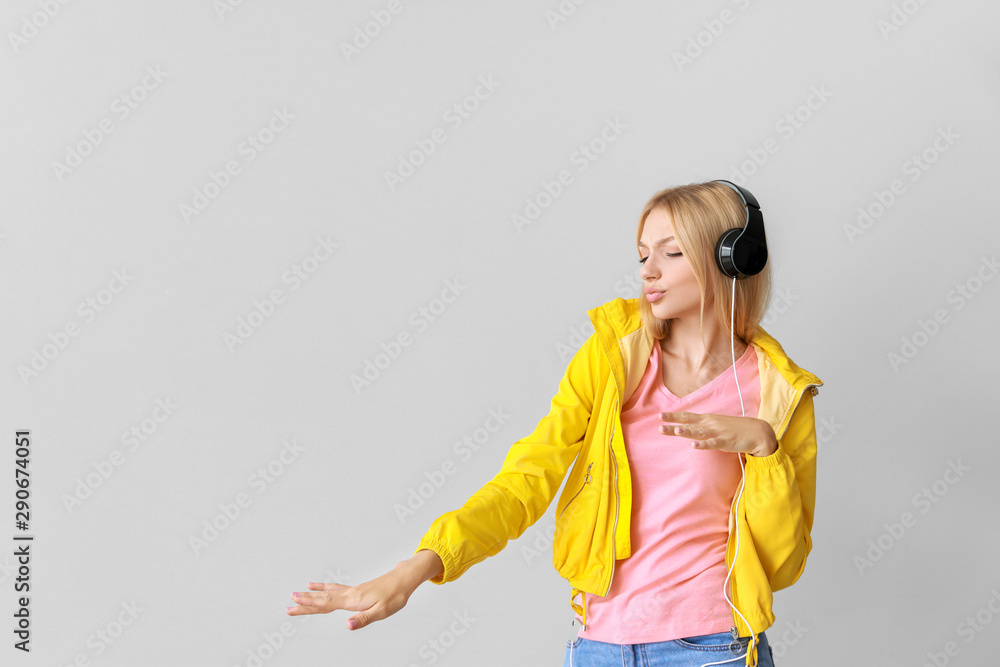 Beautiful young woman listening to music on light background