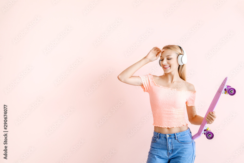 Beautiful young woman with skateboard listening to music on color background