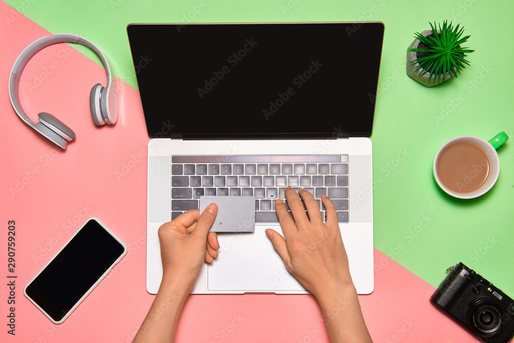 Young man with credit card using laptop for online shopping on color background