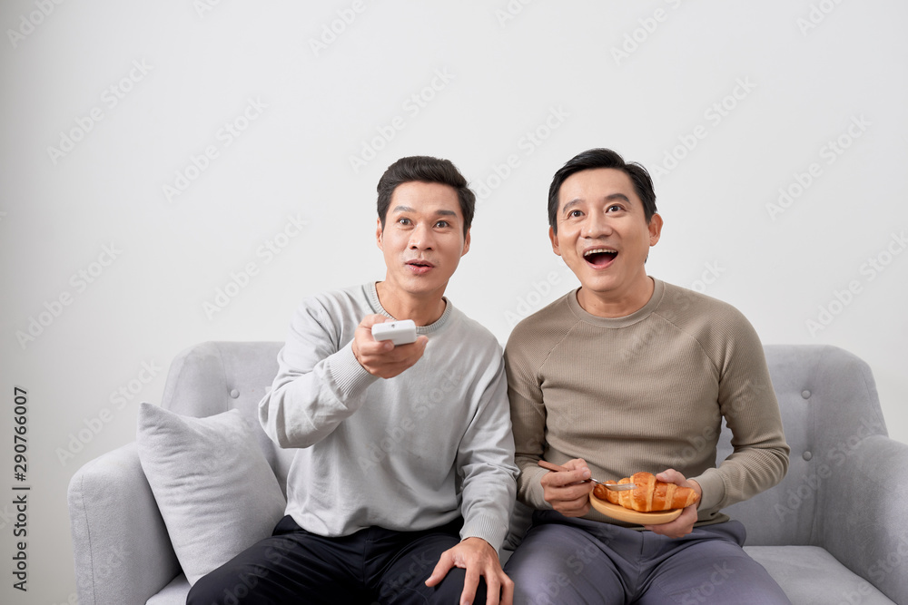 Men sitting on couch watching movie on television together at home.