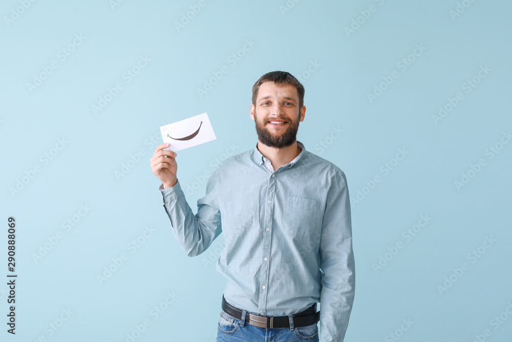 Happy man holding sheet of paper with drawn smile on color background