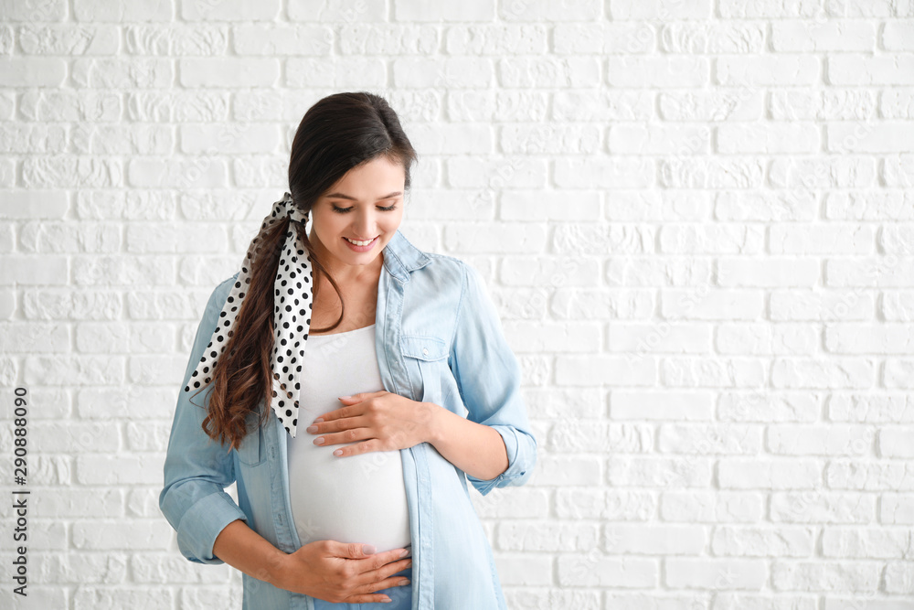 Young pregnant woman against white brick wall