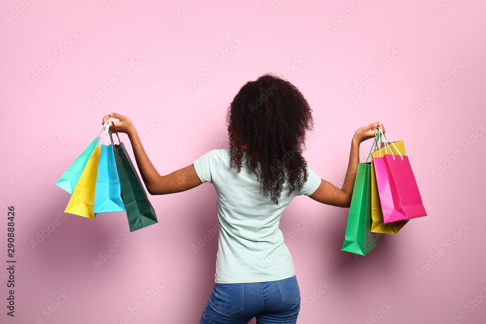 Beautiful African-American woman with shopping bags on color background, back view