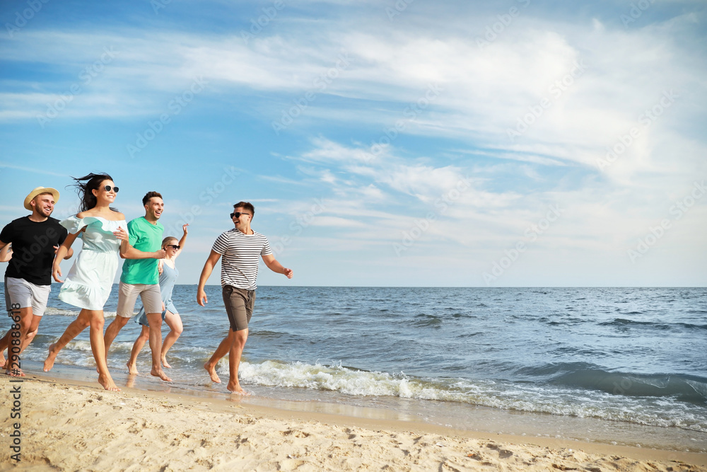 Happy friends running on sea beach at resort