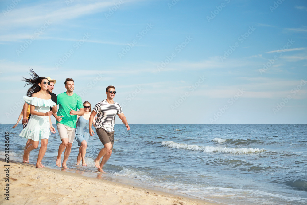 Happy friends running on sea beach at resort