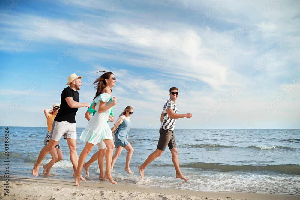 Happy friends running on sea beach at resort