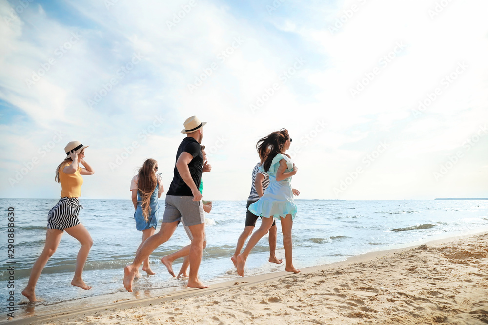 Happy friends running on sea beach at resort