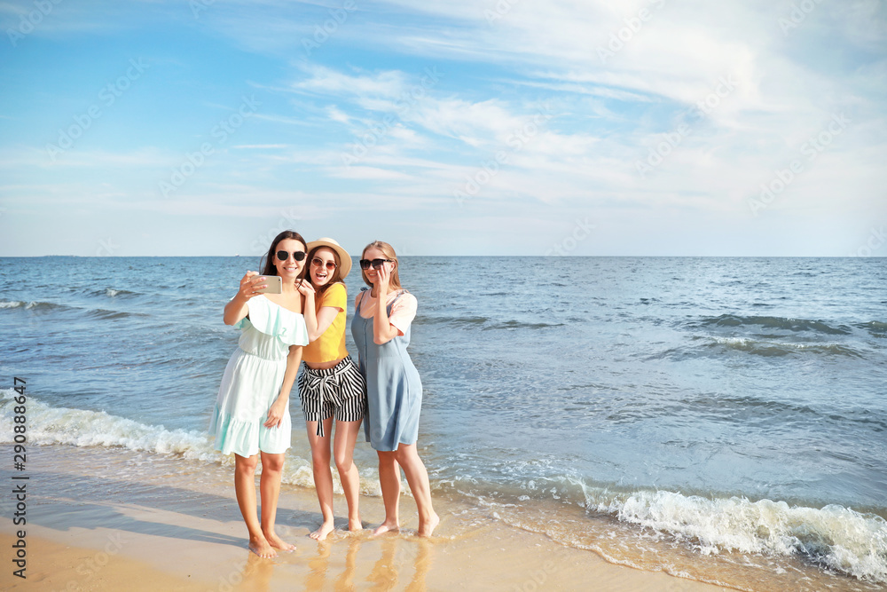 Happy young women taking selfie on sea beach at resort