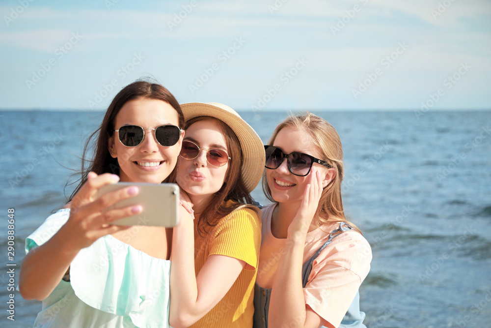 Happy young women taking selfie on sea beach at resort