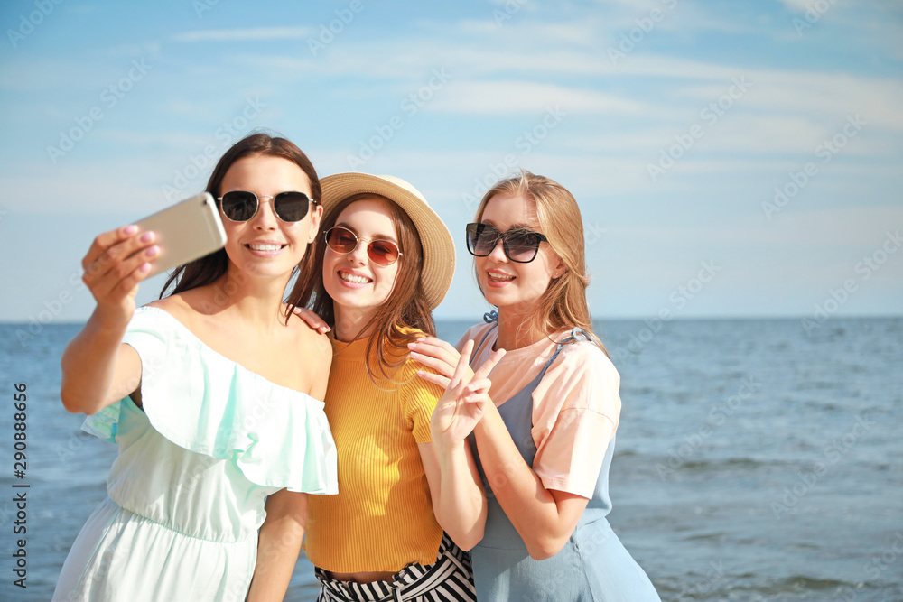 Happy young women taking selfie on sea beach at resort