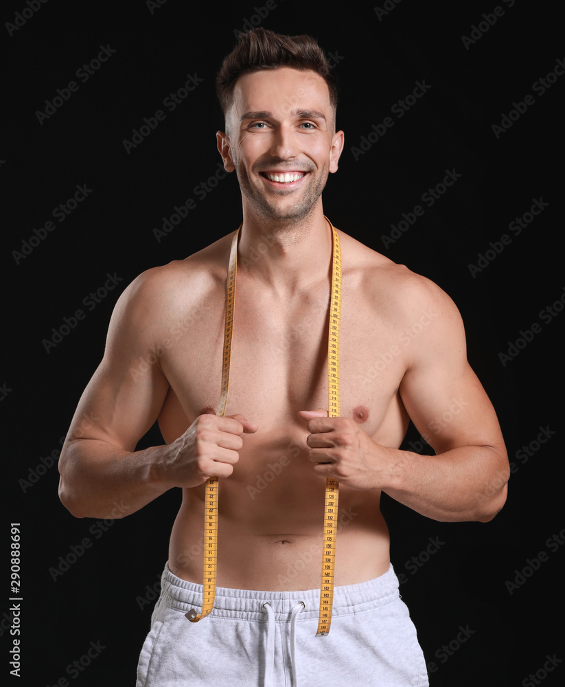 Handsome muscular man with measuring tape on dark background. Weight loss concept