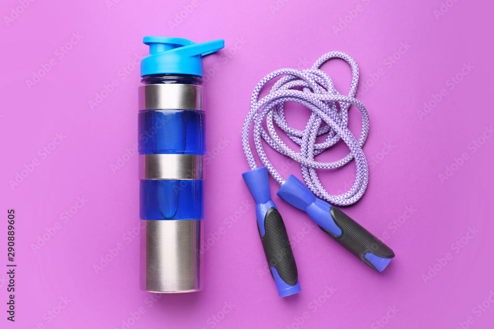 Sports water bottle and jumping rope on color background