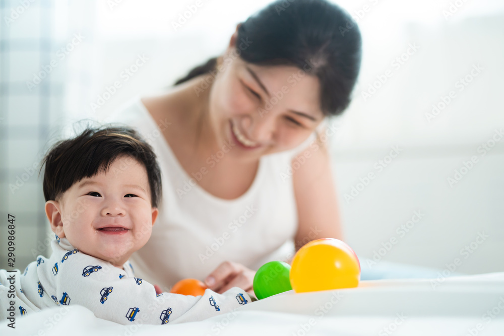 Asian cute mother and baby playing colorful ball on the bed. Mom touching her kid while the child is