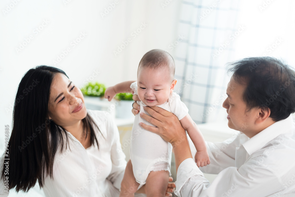 Asian parents holding and playing with newborn baby in bedroom. Father holding son in hand and Mothe