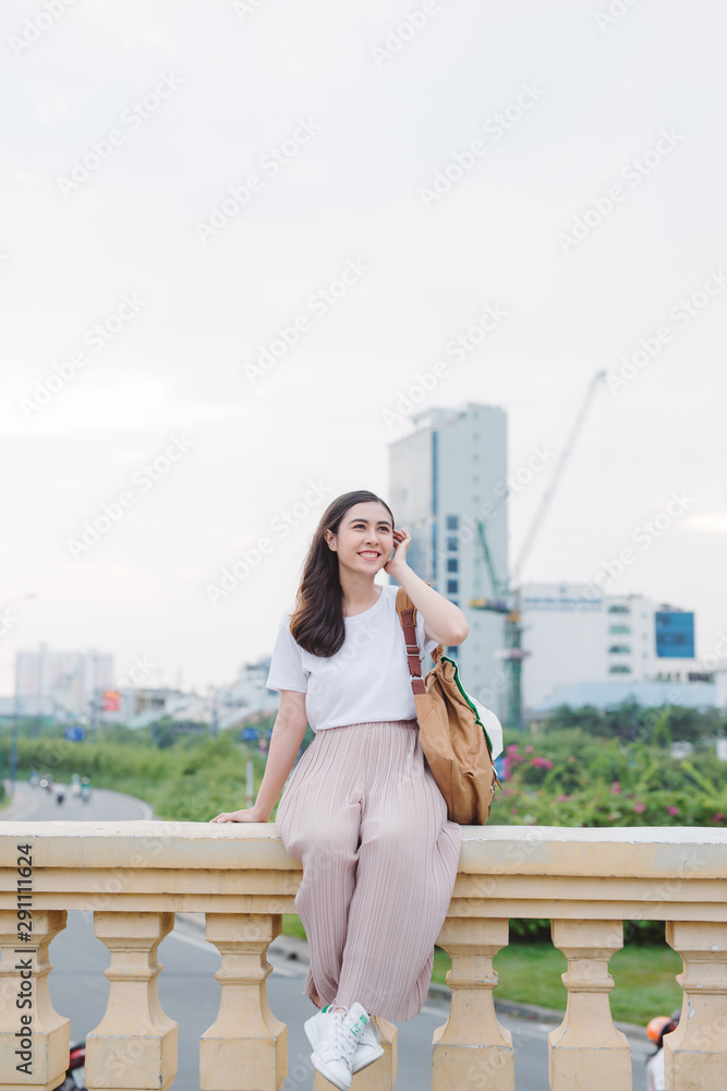 可爱的女孩坐在桥栏杆上。享受河流的美丽。独自坐着看。