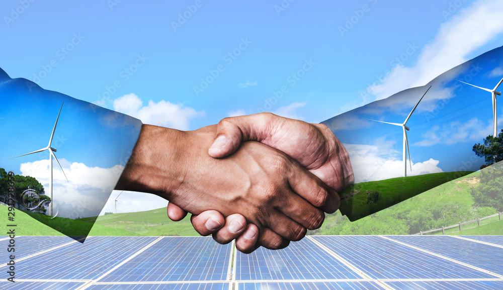 Double exposure graphic of business people handshake over wind turbine farm and green renewable ener