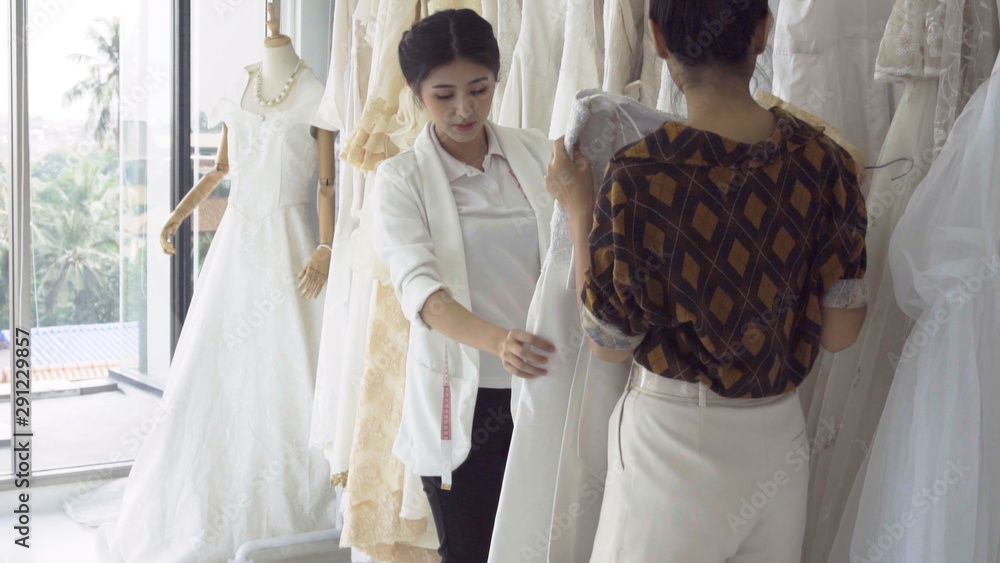 Future bride customer talking with wedding store shopkeeper to buy wedding dress and accessories for