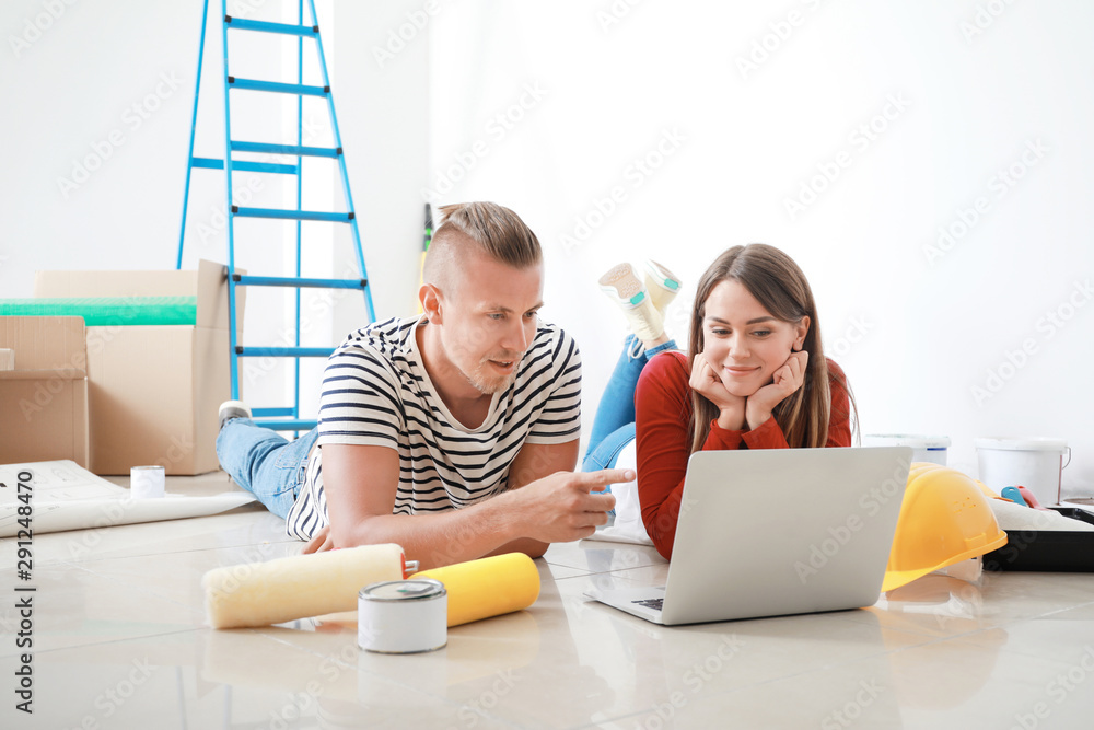 Happy young couple with laptop planning repair in their new house