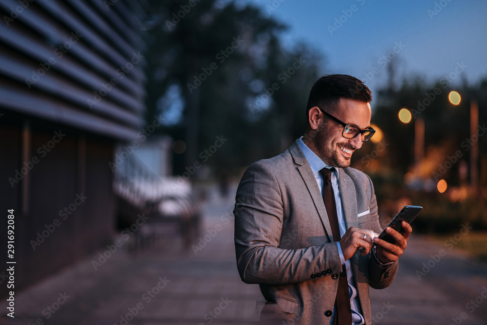 Portrait of a smiling executive using smart phone in the evening outdoors.