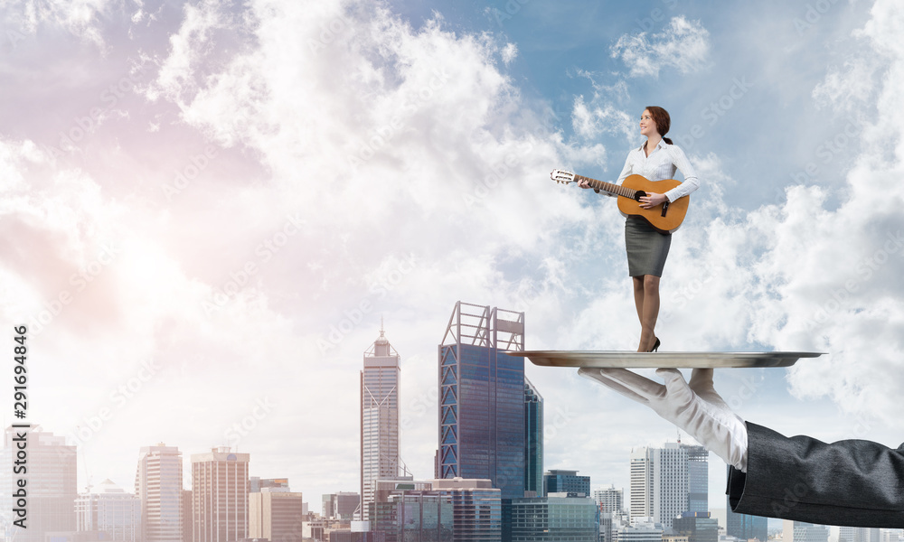 Attractive businesswoman on metal tray playing acoustic guitar against cityscape background