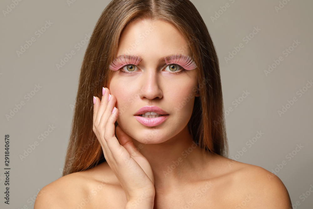 Young woman with creative eyelashes on grey background