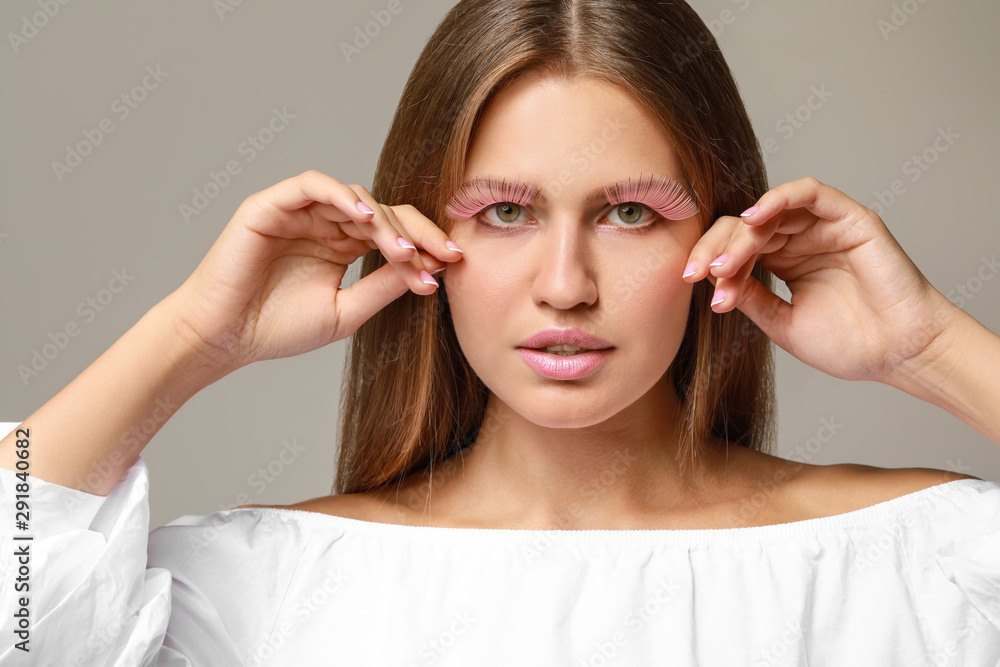 Young woman with creative eyelashes on grey background