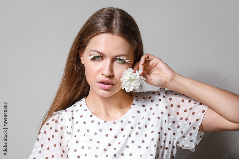 灰色背景下有创意睫毛和花朵的年轻女性