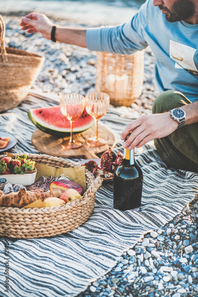 Summer beach picnic at sunset. Young couple sitting on blanket having weekend picnic outdoor at seas