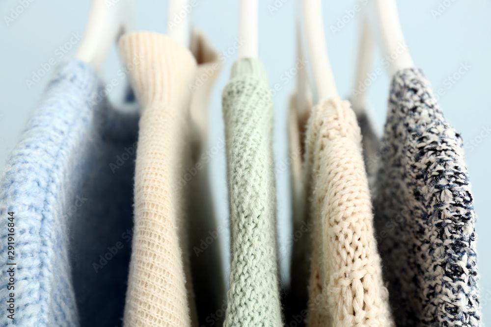 Hangers with winter clothes on color background, closeup