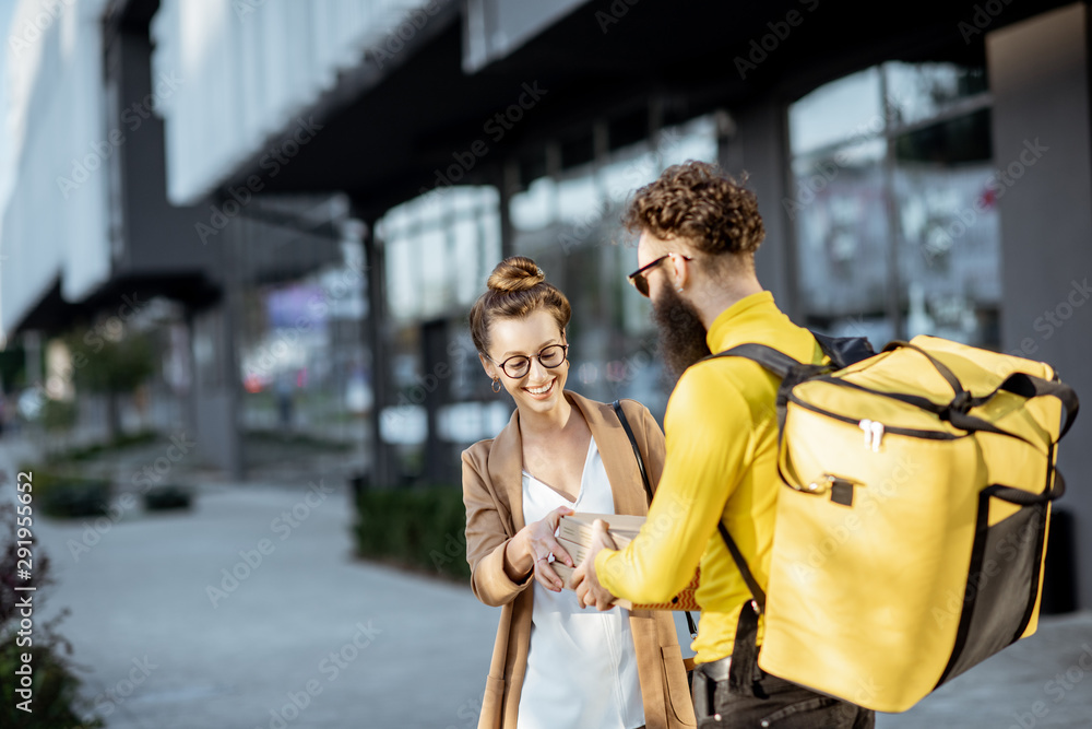 男快递员用保温袋给一位年轻的女商人送披萨，站在附近