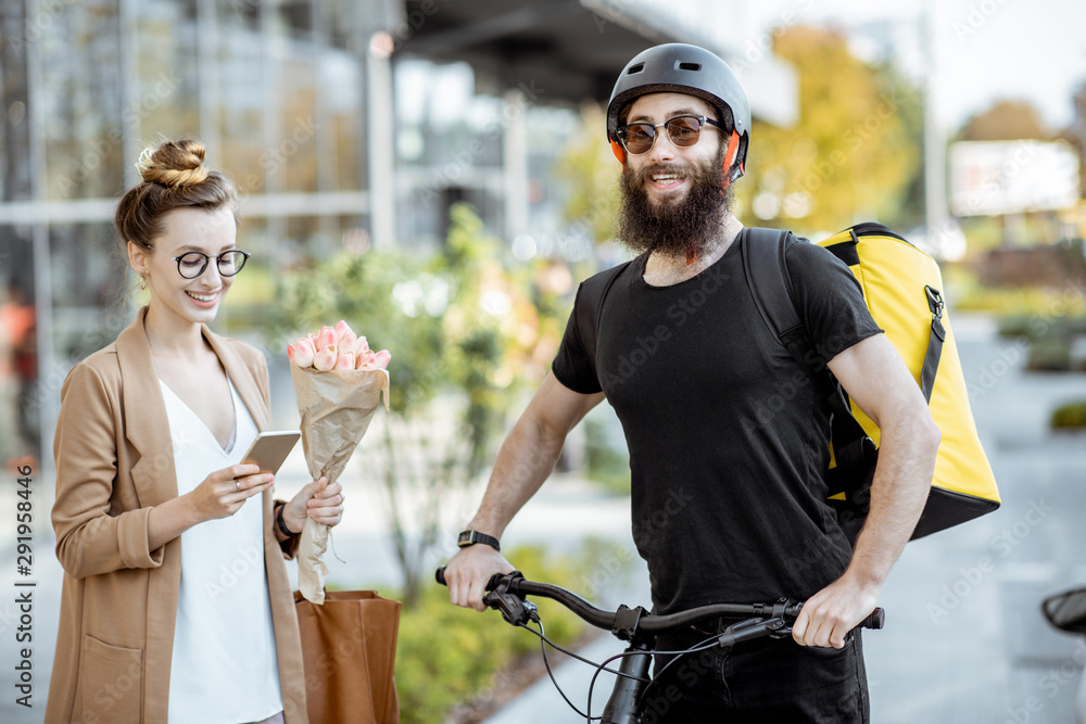 Courier delivering fresh flowers to a young business woman on a bicycle wearing delivery backpack. F