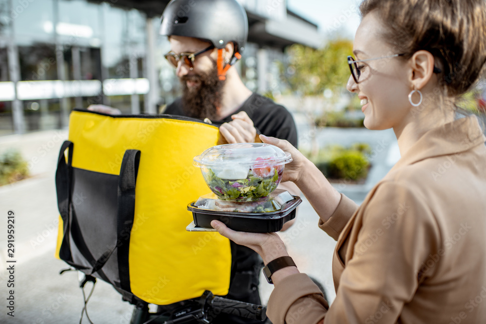 Courier delivering fresh lunches to a young business woman on a bicycle with thermal backpack. Takea