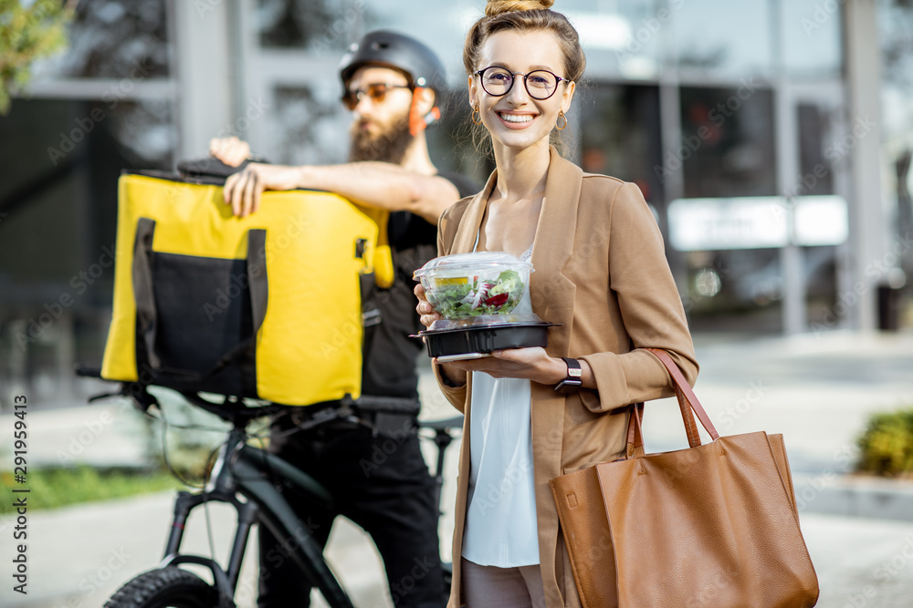 Happy businesswoman receiving fresh takaway lunches, standing near the office building with a male c