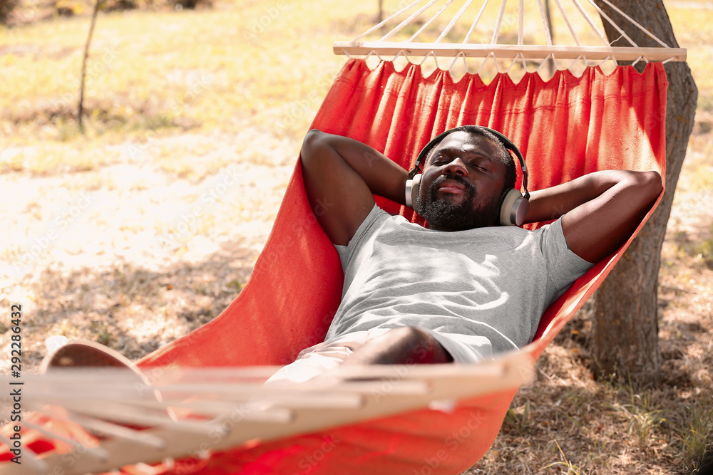 African-American man listening to music while relaxing in hammock outdoors