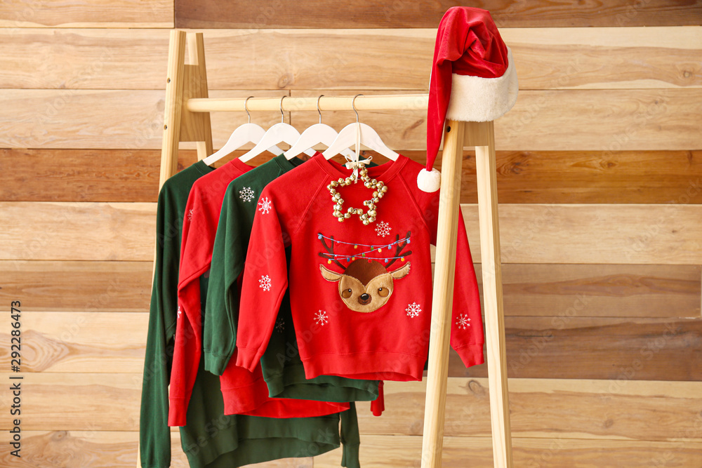 Rack with Christmas clothes on wooden background