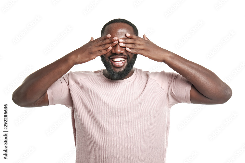 Handsome African-American man covering his eyes on white background