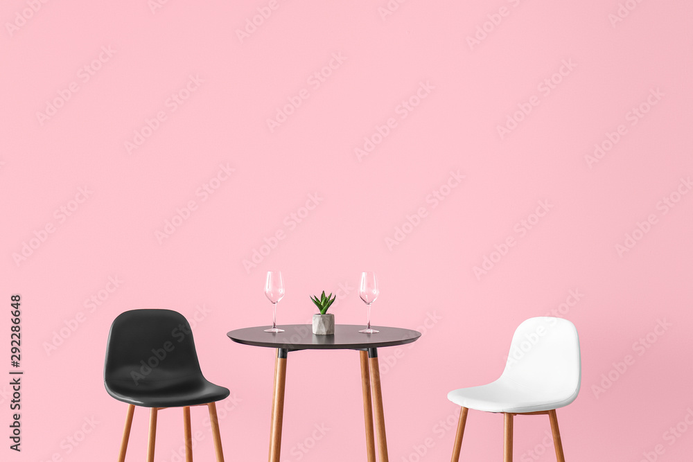 Chairs and table with empty glasses near color wall