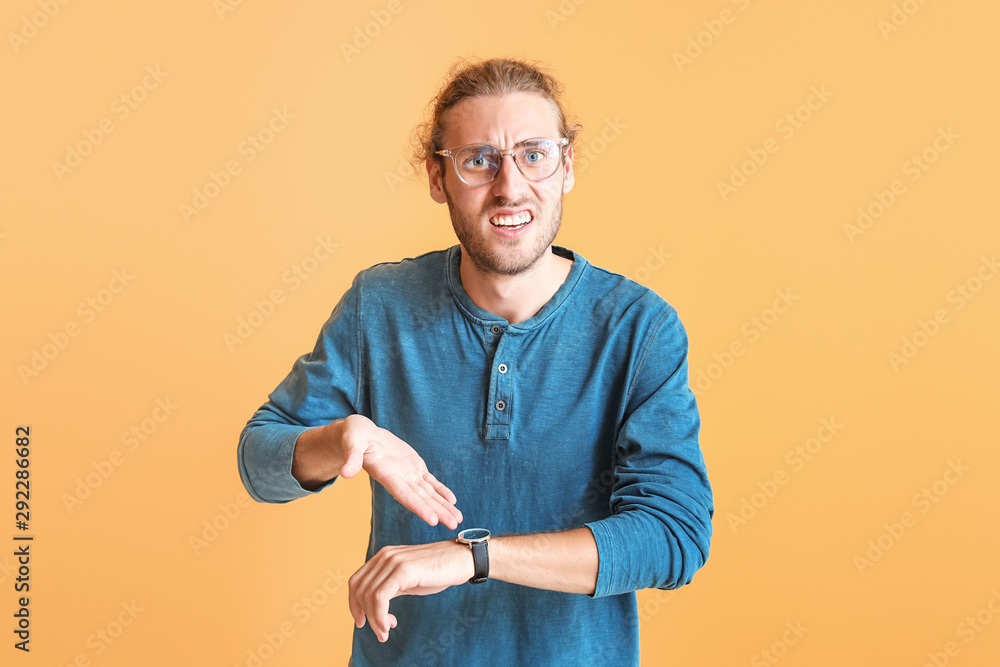 Stressed young man with watch on color background