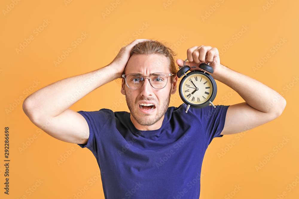 Stressed man with alarm clock on color background