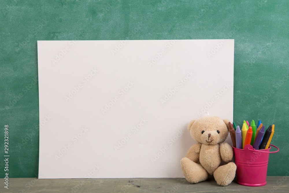 colored crayons and toy bear on the wooden table - elementary school education concept, chalkboard b