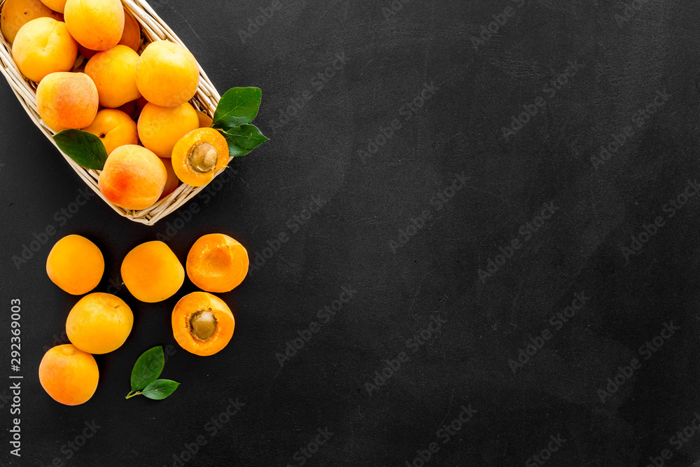 Fresh raw apricots in basket on black background top view pattern with leaves