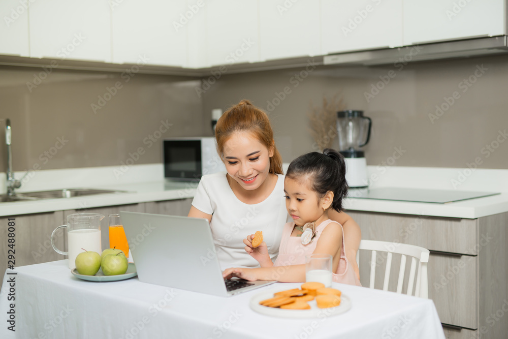 年轻的父母和他们的女儿坐在桌子旁，用笔记本电脑看东西。