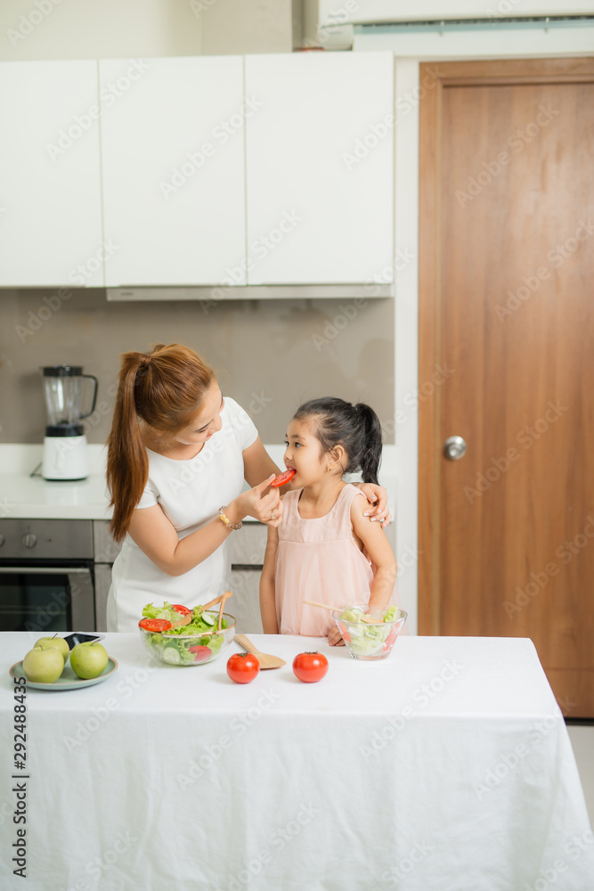 Cute little girl and her mom in chefs hats are cutting vegetables cooking a salad and smiling