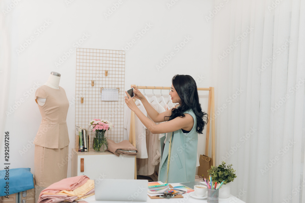 Young Asian female fashion designer taking measurements on mannequin in her studio