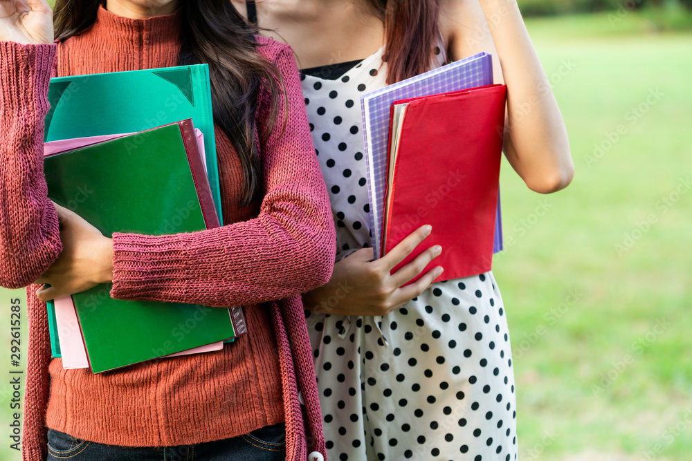 年轻的女学生朋友站在大学公园里手里拿着书。教育总结