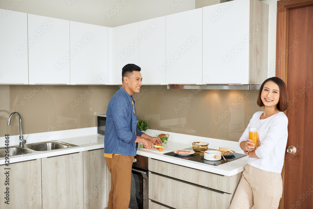 年轻夫妇吃早餐，女人拿着橙汁，男人烹饪食物厨房现代公寓